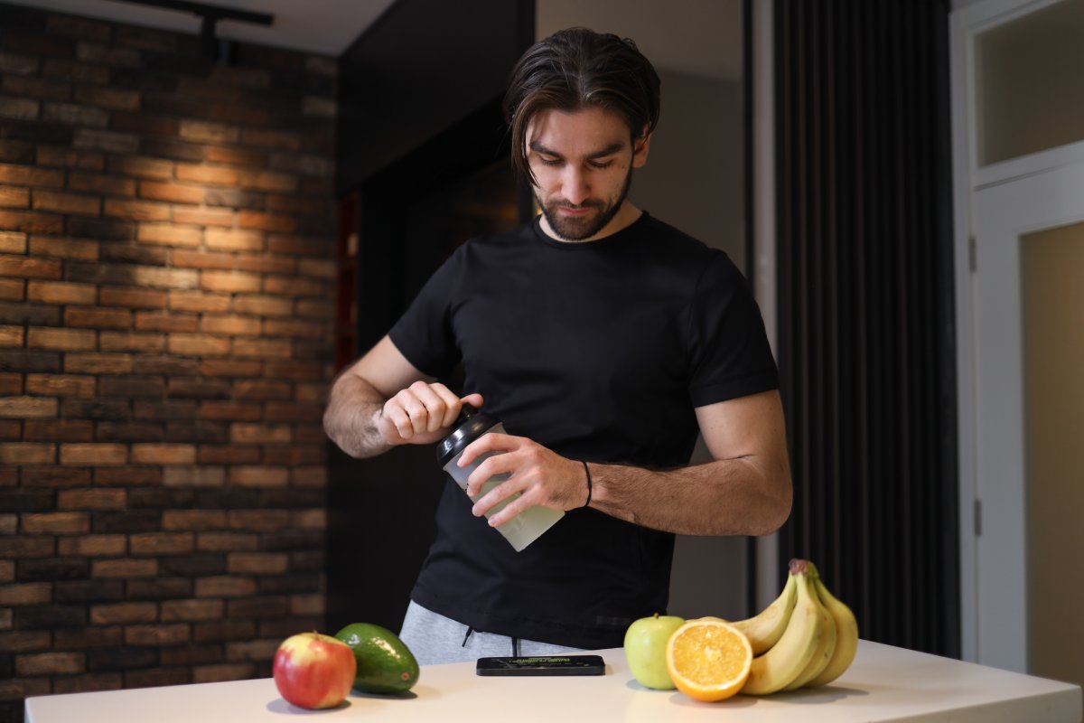 Sportista pije šejk dok čita o pre-workout suplementima na telefonu.