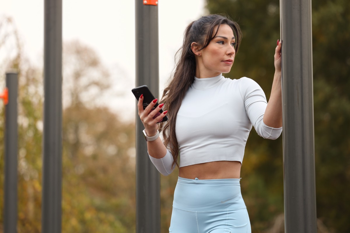 Devojka u sportskoj opremi drži telefon i odmara nakon kardio vežbi